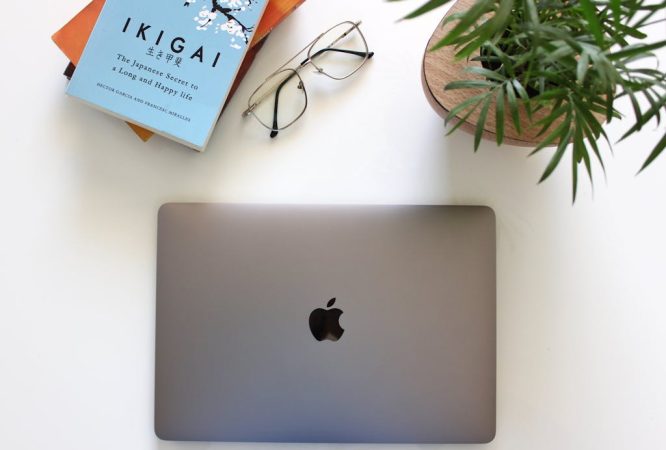 Apple MacBook next to Eyeglasses and Stack of Books