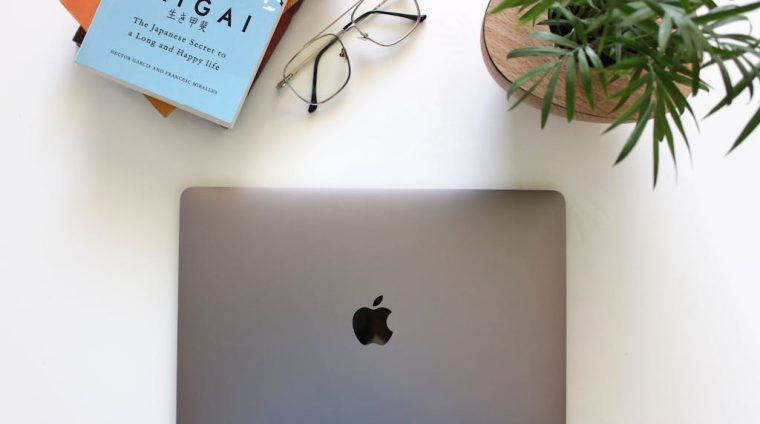 Apple MacBook next to Eyeglasses and Stack of Books