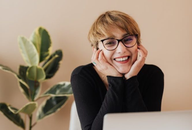 Cheerful woman smiling while sitting at table with laptop