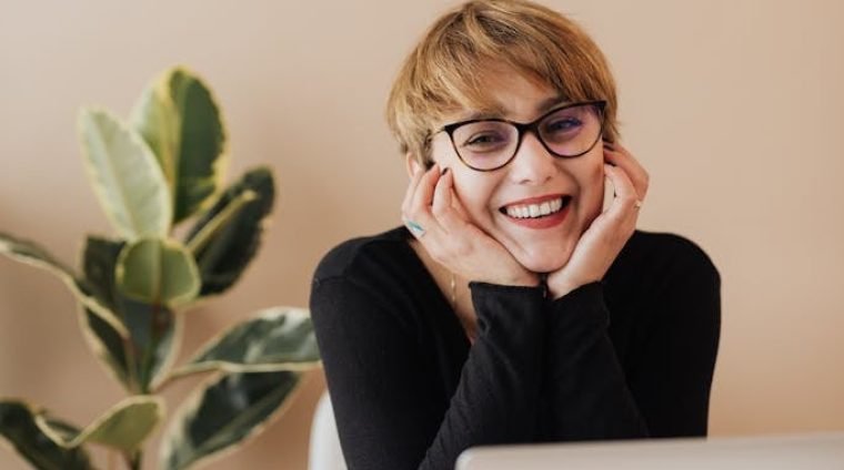 Cheerful woman smiling while sitting at table with laptop