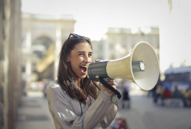 Cheerful young woman screaming into megaphone