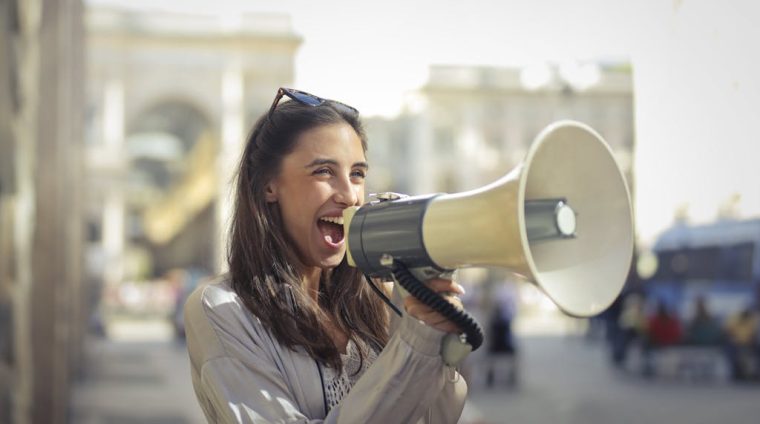 Cheerful young woman screaming into megaphone