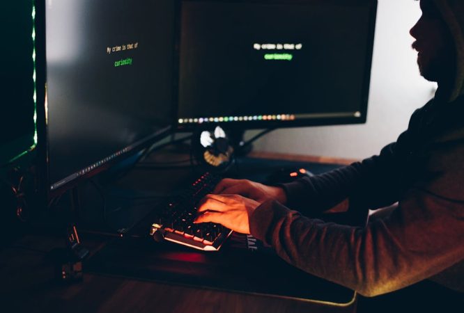 Crop hacker silhouette typing on computer keyboard while hacking system