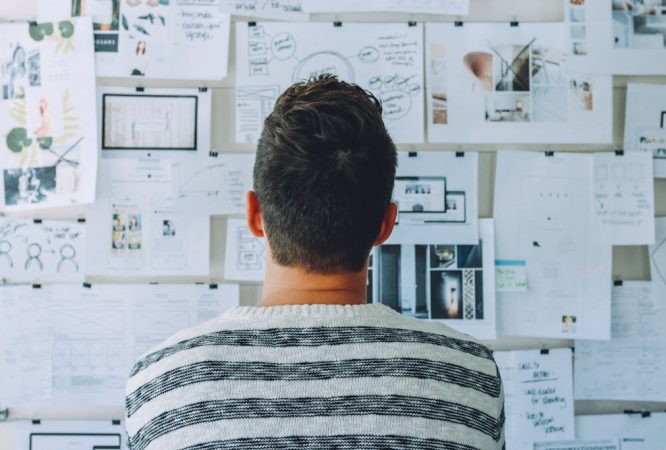 Man Wearing Black and White Stripe Shirt Looking at White Printer Papers on the Wall