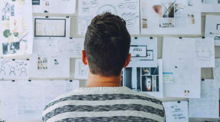 Man Wearing Black and White Stripe Shirt Looking at White Printer Papers on the Wall