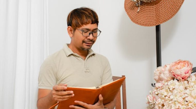 Photo of a Man Sitting on a Wooden Chair while Reading a Book