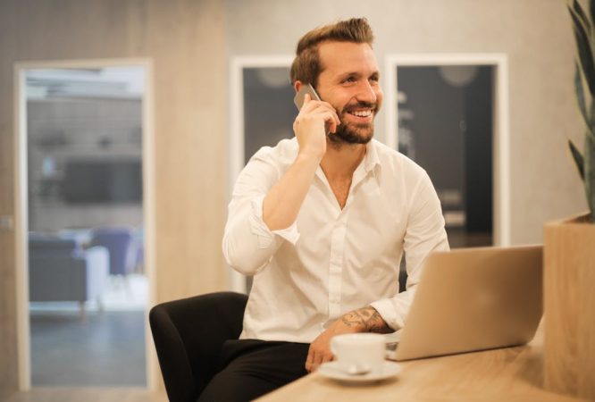 Smiling formal male with laptop chatting via phone