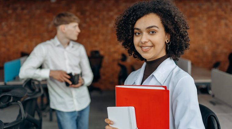 Young Woman in White Long Sleeve Shirt Holding Financial Book Report and Standing with Her Colleagues Inside an Office